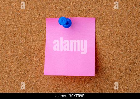 A blank pink sticky note is pinned to a brown cork board with a space for a customizable message, reminder, or memo. Stock Photo