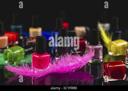 Colourful nail polish bottles and coloured feathers on black surface with reflection Stock Photo