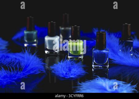 Nail polish bottles in shades of blue and green with blue feathers on a black surface with reflection Stock Photo