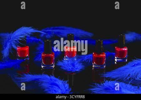 Red nail polish bottles surrounded by blue feathers on a black surface with reflection Stock Photo