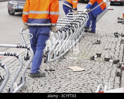 Three men in orange and blue jackets are working on a row of metal racks Stock Photo