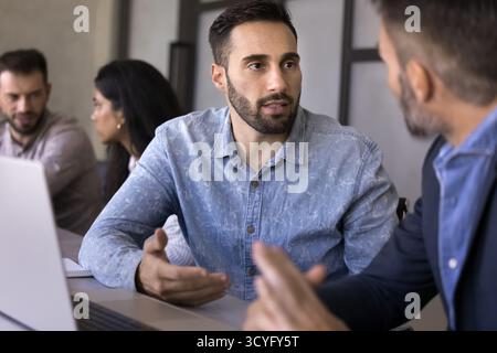 Serious millennial businessman consult male colleague by notebook screen Stock Photo