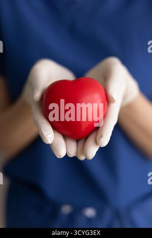 Close-up cropped image of female nurse gently holds red heart Stock Photo