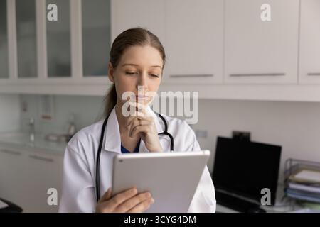 Young thoughtful woman nurse, healthcare specialist working on tablet Stock Photo