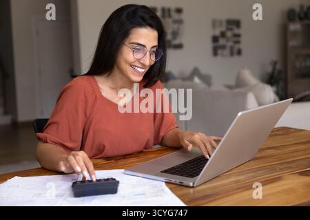 Happy young Latin accountant woman in glasses calculating monthly budget Stock Photo