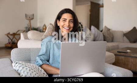 Cheerful beautiful young Latin woman using laptop at home Stock Photo