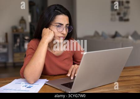 Puzzled doubting Hispanic freelancer woman thinking on problem at laptop Stock Photo