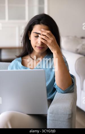 Stressed frustrated Latin freelance woman touching head with shut eyes Stock Photo