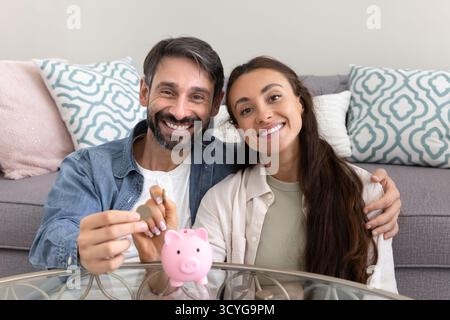 Happy millennial husband wife prepare to drop coins to piggybank Stock Photo