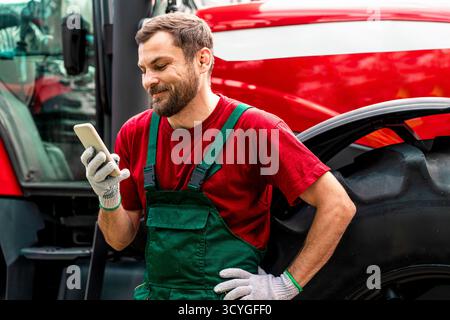 Male farmer standing by tractor using mobile phone and smiling. Stock Photo