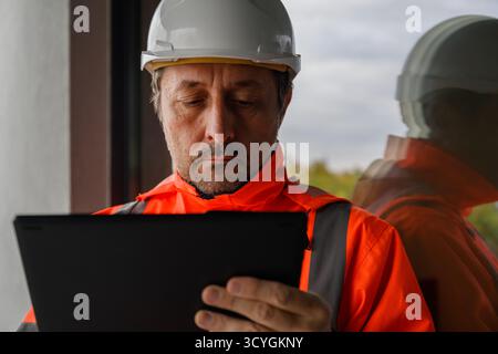 Civil engineer wearing safety vest and hardhat inspecting project data on digital tablet, concept of smart construction, innovation, and modern engine Stock Photo