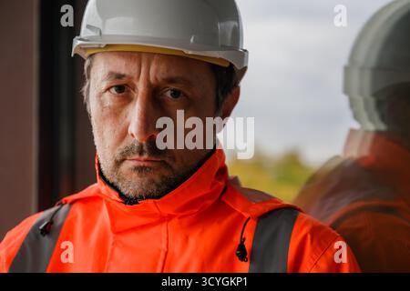 Confident civil engineer wearing white hardhat looking at camera at construction site, symbol of professionalism and responsibility in engineering. Se Stock Photo
