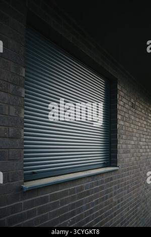 Closed metal roller shutter on a modern brick wall, security and privacy concept. Selective focus. Stock Photo