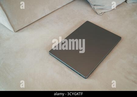 Closed laptop resting on living room sofa, symbolizing end of remote work, digital break, or modern home office lifestyle. Selective focus. Stock Photo