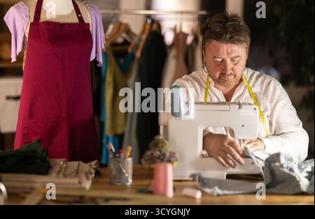 Middle-aged male dressmaker working with sewing-machine Stock Photo