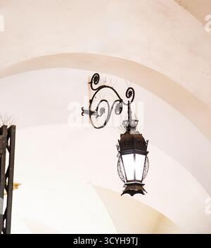 An old wrought iron street lamp under a vaulted ceiling, with space for an inscription. Stock Photo