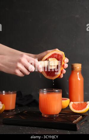 Young woman squeezing grapefruit with wooden juicer into glass on black background Stock Photo