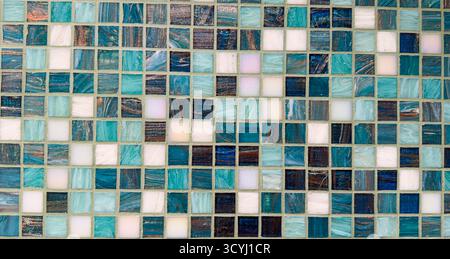 Decorative wall of glass mosaic tiles in shades of blue, teal, and white with reflective texture. Stock Photo