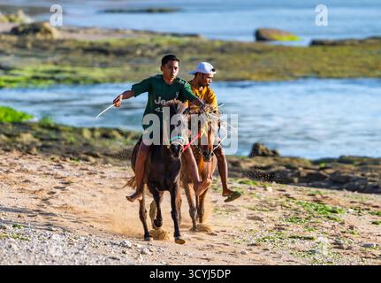 Two young men racing their horses on the beach. Rote, Indonesia. Stock Photo