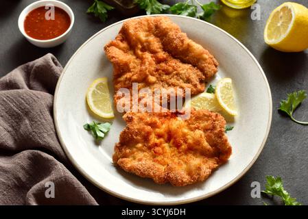 Schnitzel with served with lemon and parsley on white plate on brown stone background. Close up view Stock Photo