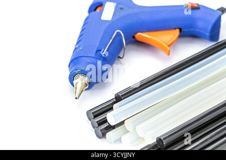 A blue hot glue gun placed beside black and white glue sticks on a white background, showing essential crafting and DIY repair tools used for bonding Stock Photo