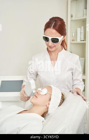 Female caucasian beautician performing laser skin treatment on young caucasian woman in spa clinic. Stock Photo