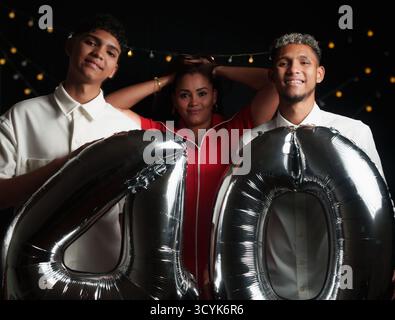 a woman dressed in red and her two children dressed in white posing for a photo with a black background and two balloons Stock Photo