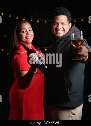 A man and a woman are holding a bottle of wine and a glass. The man is smiling and the woman is also smiling Stock Photo