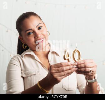 A woman is holding a candle that says 40. She is smiling. The candle is lit. The woman is wearing a white shirt Stock Photo
