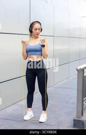 Fit woman performs sport exercise workout outdoor, using resistance band for arm stretch, developing Stock Photo