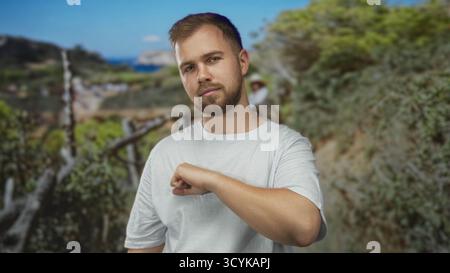 Young man with beard wearing white t shirt and fist extended toward camera in forest path; determination grit resilience. Stock Photo