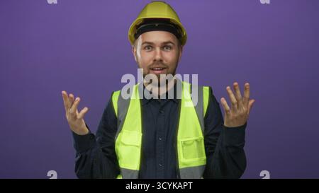Builder man wearing yellow hardhat and high visibility vest points finger to chest in purple studio; safety concern confused. Stock Photo