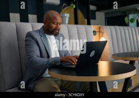 Focused mature businessman in blazer using laptop at desk in office lounge Stock Photo