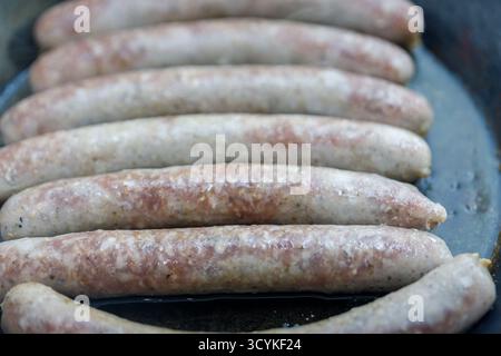 A close-up, overhead shot showcases a row of raw sausages in a pan. Their pale pink and beige tones are speckled with darker spices. Stock Photo