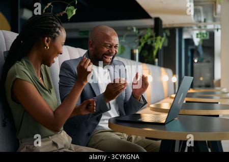 Joyful businesspeople in smart casuals laughing while sitting at desk with laptop in office lounge Stock Photo