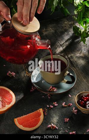 pouring herbal tea with grapefruit slices, steaming herbal tea with hibiscus petals on textured Stock Photo