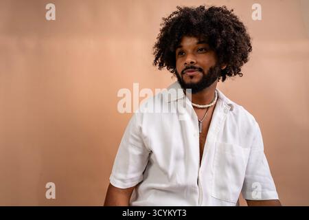 Young man wearing a white shirt and beaded necklace contemplating on a neutral background Stock Photo
