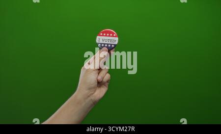 Man holding voting badge against green background symbolizes civic engagement in elections showing hand and pin. Stock Photo