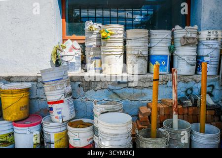 A collection of old paint buckets and tools outside a construction site with a cracked wall and a window visible in the background Stock Photo