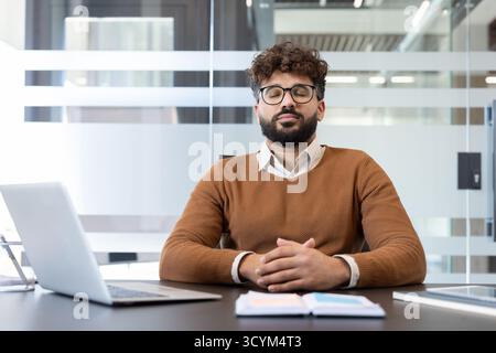 Young man meditating at his office desk, eyes closed and breathing deeply to relieve stress, promote mindfulness and calm during a busy workday in a modern workspace Stock Photo