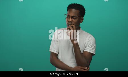 Man with finger on chin gesture in green studio, wearing eyeglasses and white polo shirt; contemplation. Stock Photo