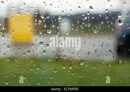 Close-up view of shimmering raindrops on window glass creating abstract patterns against blurry outdoor background. Concept of rainy weather, melancho Stock Photo