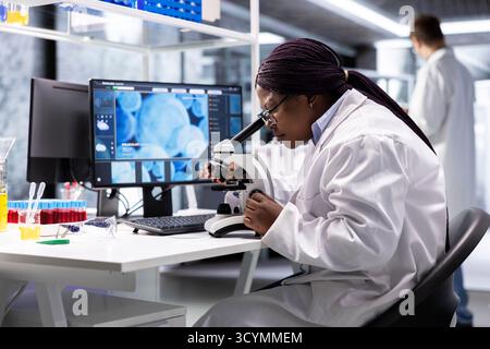 Black scientist examining samples under microscope in a modern laboratory. Research work integrates biotechnology, molecular science and advanced diagnostics to shape medical discovery. Stock Photo