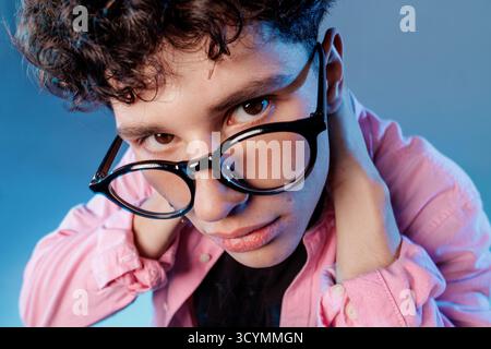 Young man in eyewear peering over frames with curious skeptical look, ideal for eyesight, optometry, tech lifestyle and health stories. Stock Photo