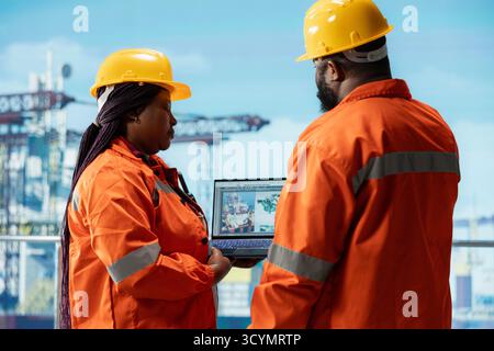 Drilling rig technicians brainstorming, using laptop software dashboard for anomaly detection during operation. Teamworking offshore platform colleagues use notebook to control systems remotely Stock Photo