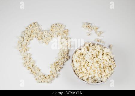 A stack of popcorn on a white table in a heart shape, denoting love for more popcorn. Stock Photo