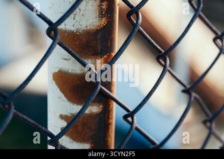 Close-up detail of a rusty metal fence post and weathered chain-link mesh Stock Photo