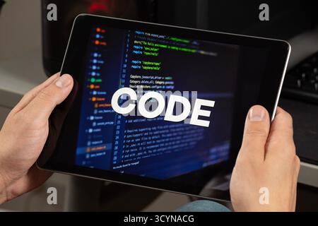 Close up to a male hands holding a tablet with the phrase code over a writing code concept Stock Photo