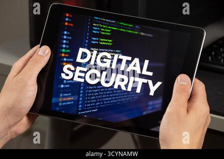 Close up to a male hands holding a tablet with the phrase digital security over a writing code concept Stock Photo