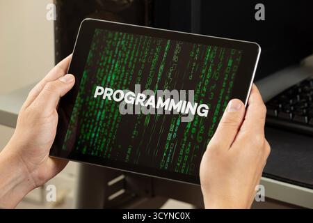 Close up to a male hands holding a tablet with the word programming over a green matrix code concept Stock Photo